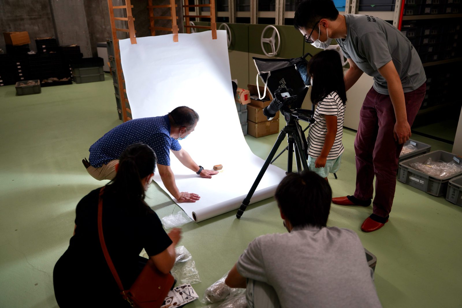 収蔵庫で白背景を敷き、石棒を撮影する参加者たち